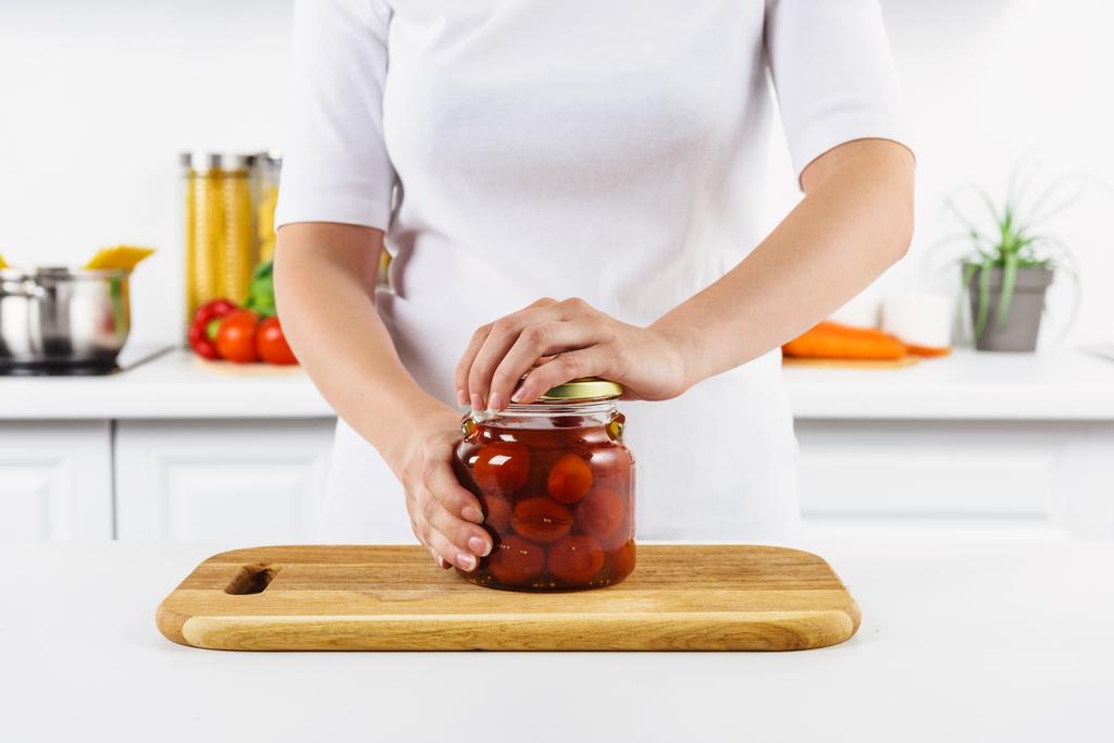 abgeschnittenes Bild einer Frau, die in heller Küche ein Glas mit eingelegten Tomaten öffnet - Foto, Bild