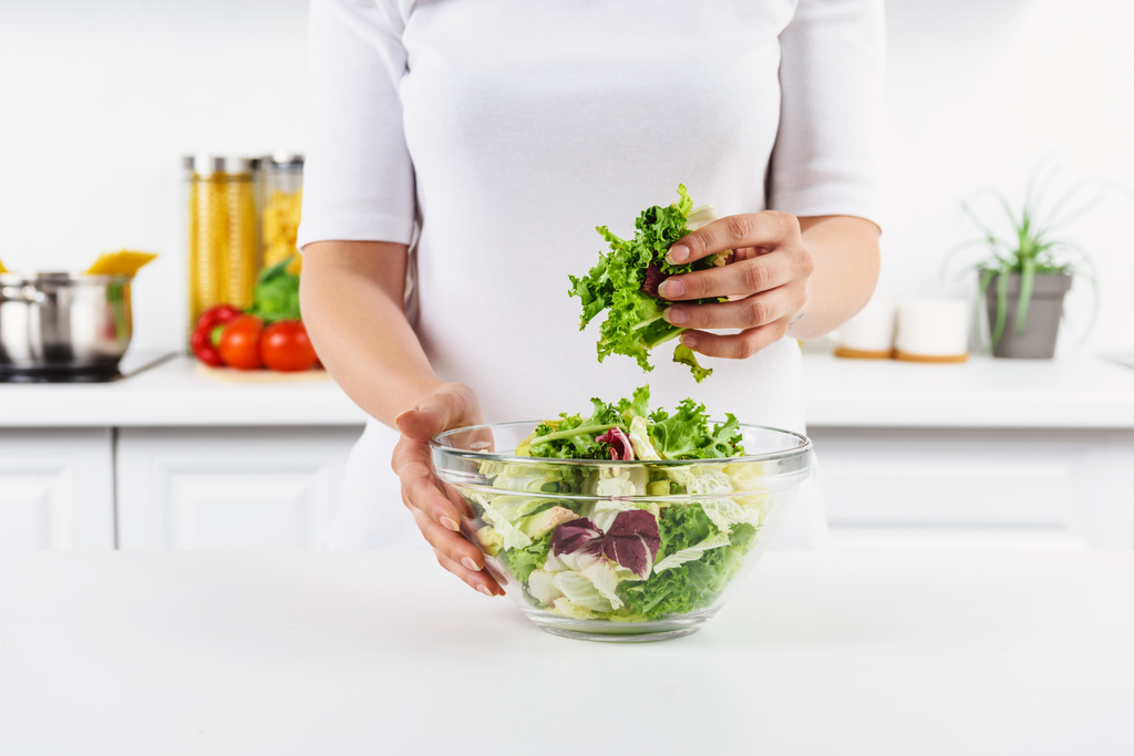 περικομμένη εικόνα γυναίκας που κρατά μπολ με σαλάτα αφήνει στην ελαφριά κουζίνα - Φωτογραφία, εικόνα