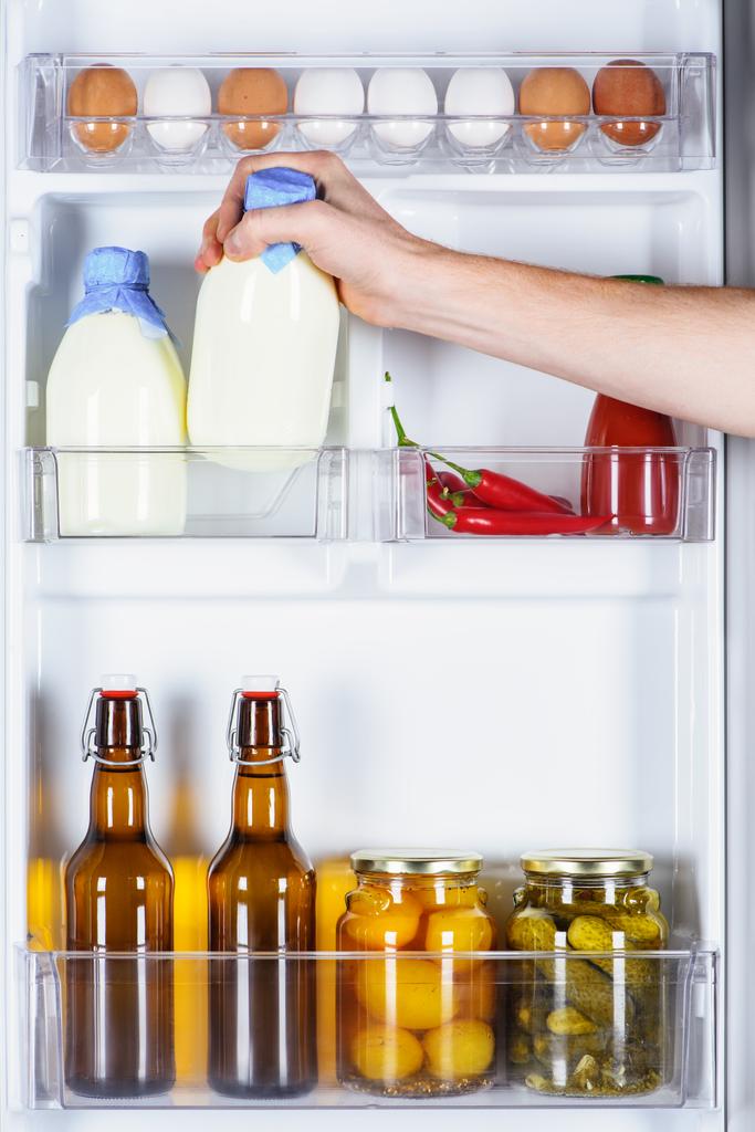 abgeschnittenes Bild eines Mannes, der eine Flasche Milch aus dem Kühlschrank nimmt - Foto, Bild