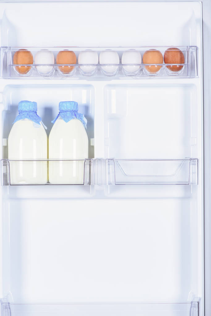 Kippeneieren en flessen van melk in de koelkast - Foto, afbeelding