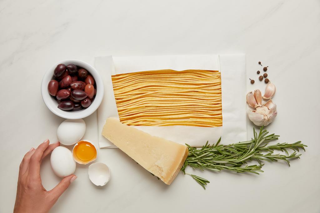 částečný pohled ženy a italské těstoviny ingredience na bílé mramorové stolní - Fotografie, Obrázek