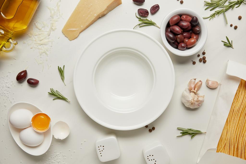 επίπεδη lay με άδειο πιάτο και ζυμαρικά συστατικά σε λευκή μαρμάρινη επιφάνεια - Φωτογραφία, εικόνα