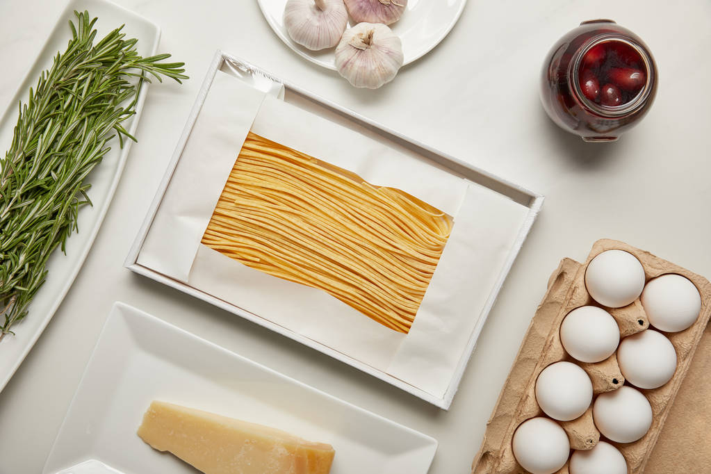 vista dall'alto di disposizione di maccheroni crudi, aglio, rosmarino e formaggio per la cottura della pasta su tavolo bianco
 - Foto, immagini