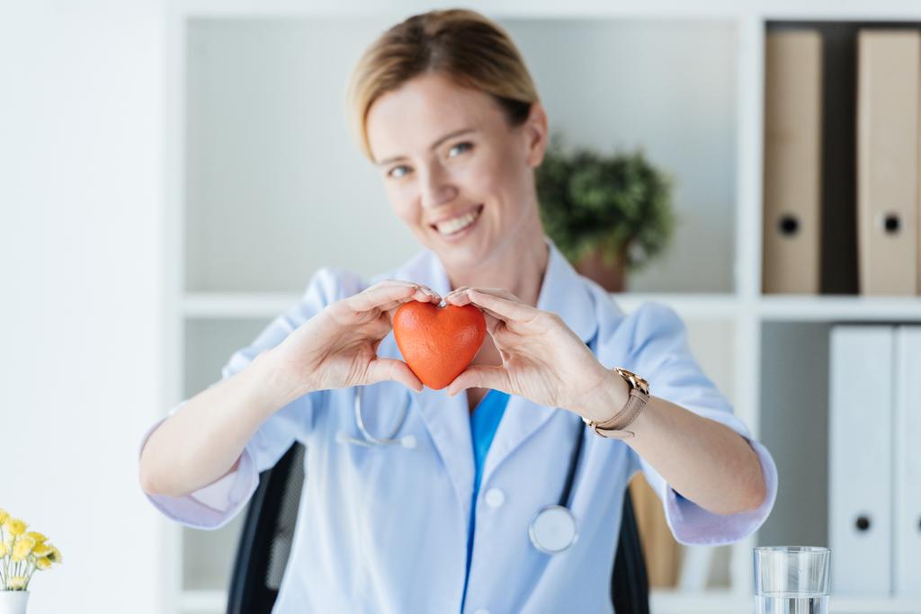 вибірковий фокус жінки-лікаря в білому пальто, що показує символ серця за столом в офісі
  - Фото, зображення