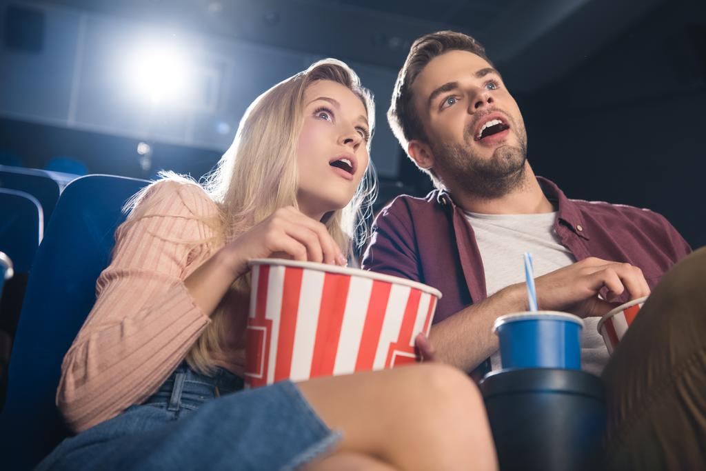 ポップコーンとソーダでショックを受けたカップルが映画館で映画を見る一緒に飲む - 写真・画像