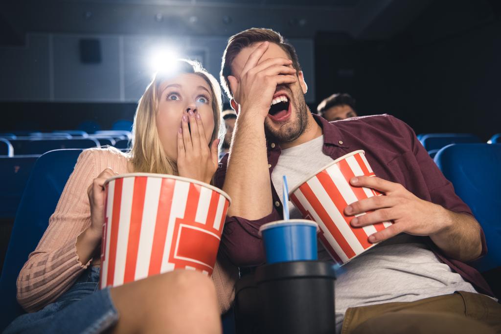 scared couple with popcorn and soda drink watching film together in cinema - Photo, Image