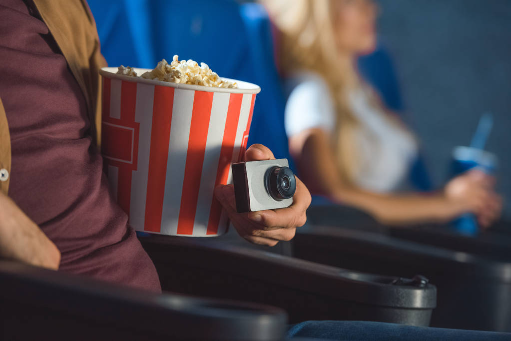 Mann mit kleiner Videokamera und Popcorn filmt illegal Film im Kino - Foto, Bild