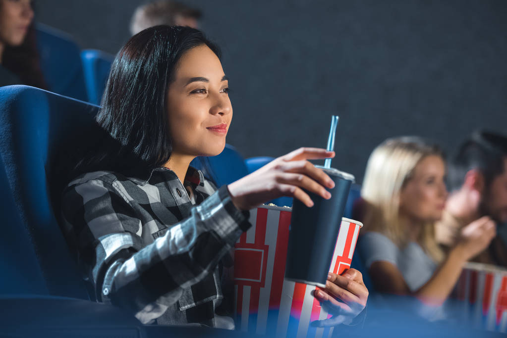 вид сбоку улыбающейся женщины с кукурузой и газировкой, смотрящей кино в кинотеатре
 - Фото, изображение