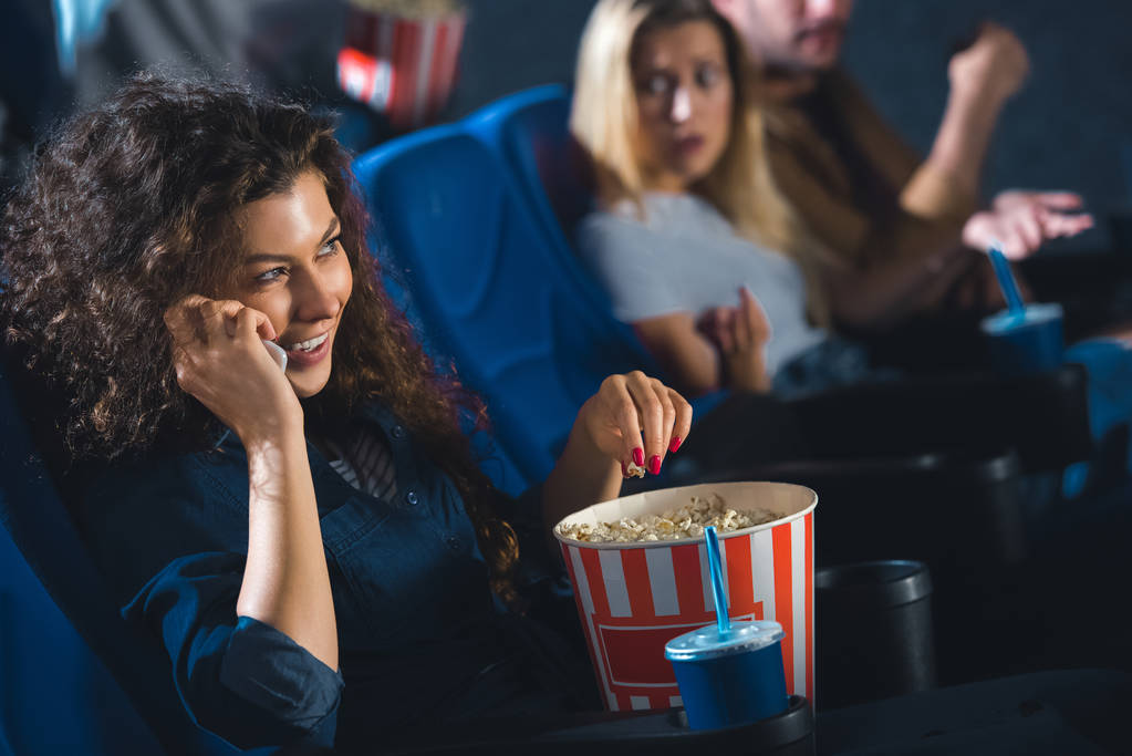 Frau mit Popcorn spricht auf Smartphone, während sie Film im Kino anschaut - Foto, Bild