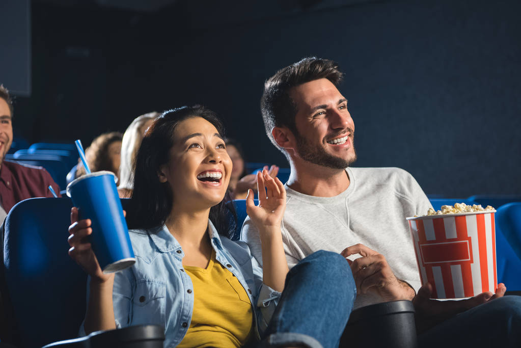 glückliches gemischtrassiges Paar mit Popcorn und Limo-Drink beim gemeinsamen Filmgucken im Kino - Foto, Bild