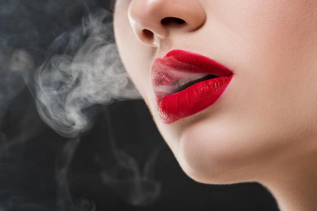 vista cortada de menina com lábios vermelhos soprando fumaça, isolado em cinza
 - Foto, Imagem