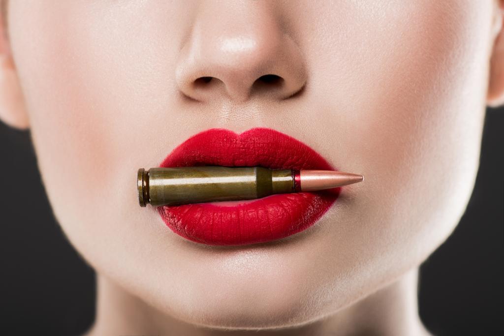 cropped view of woman holding bullet in red lips, isolated on grey - Photo, Image