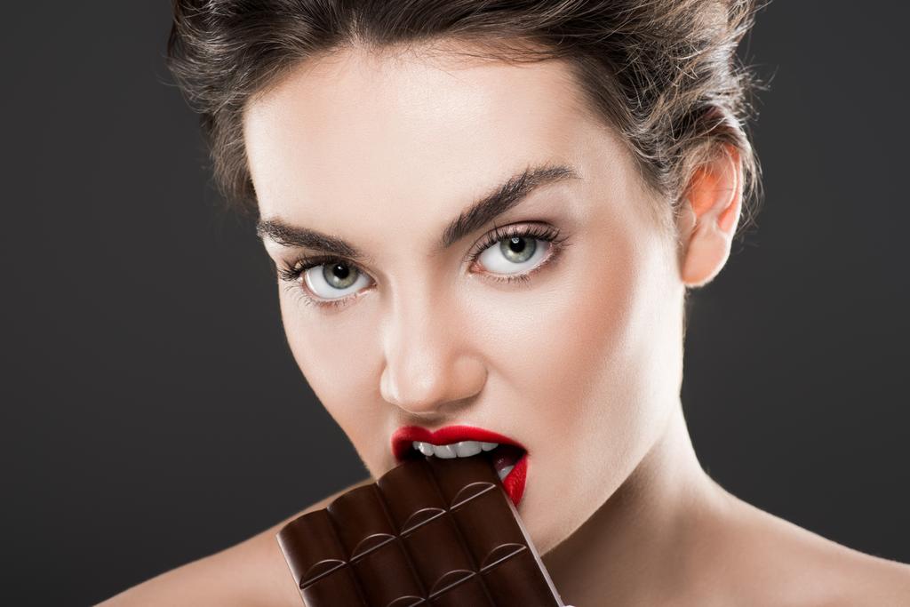 aantrekkelijke vrouw bijten chocoladereep, geïsoleerd op grijs - Foto, afbeelding