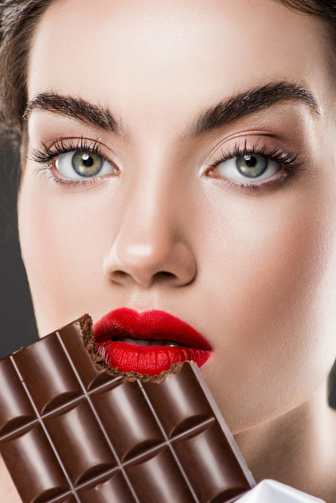 attractive girl with red lips eating chocolate bar, isolated on grey - Photo, Image