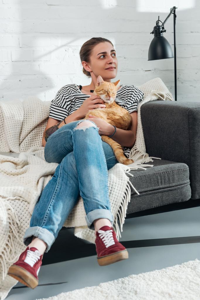 красива усміхнена дівчина погладжує червоного кота і дивиться вдома
  - Фото, зображення