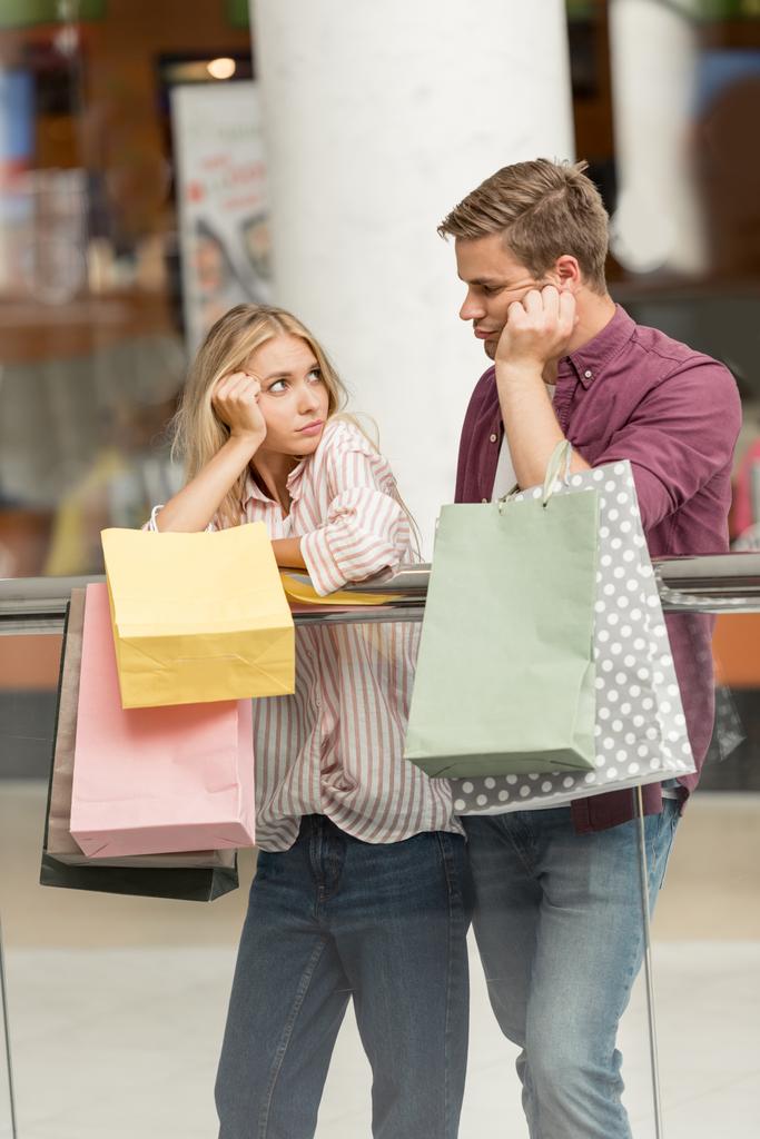 jong koppel van shoppers boos op papieren zakken kijken elkaar bij winkelcentrum  - Foto, afbeelding