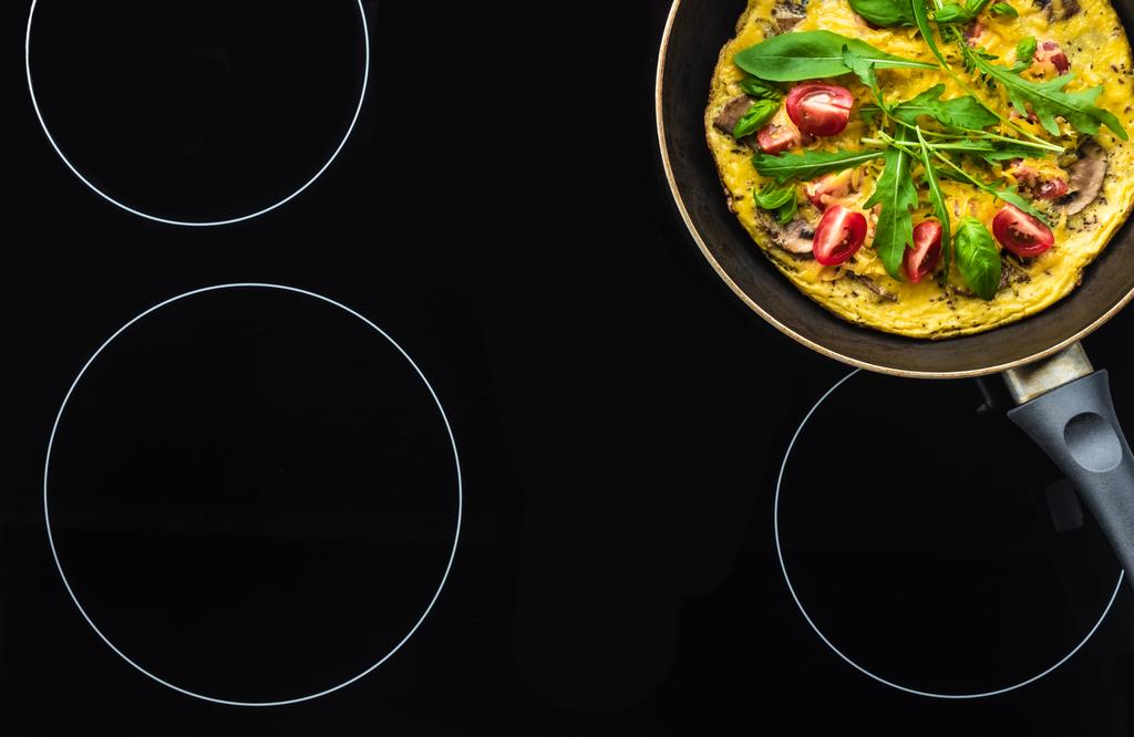 вид сверху на омлет в сковороде приготовления пищи на черной плите
 - Фото, изображение