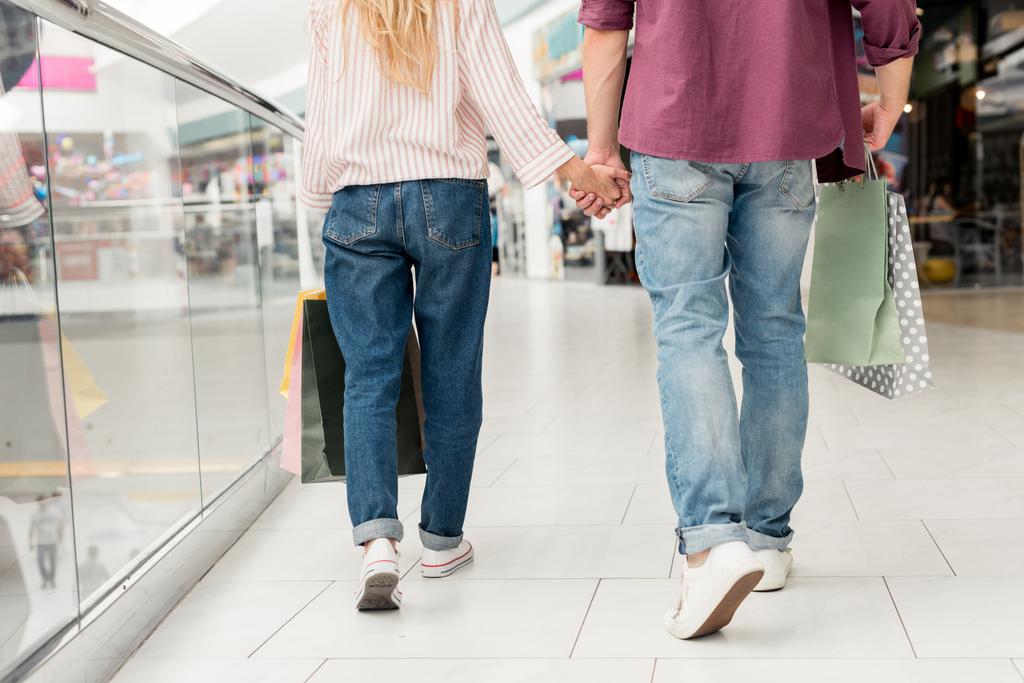 imagen recortada de un elegante par de compradores con bolsas de papel cogidas de la mano y caminando en el centro comercial
  - Foto, imagen