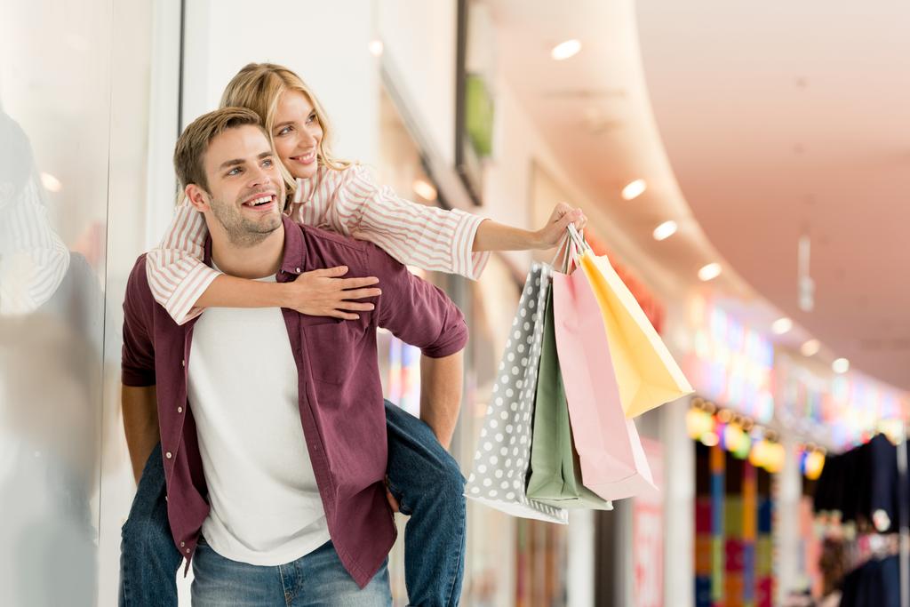  felice giovane uomo che dà cavalcata alla ragazza con borse della spesa al centro commerciale
  - Foto, immagini