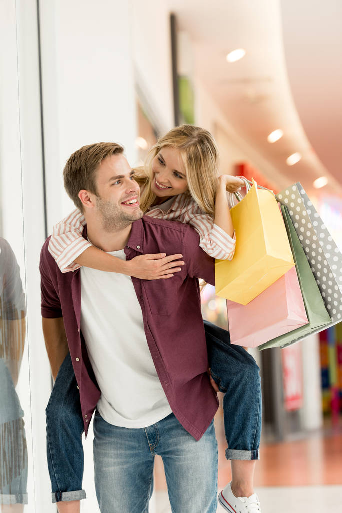 усміхнений чоловік дає стерво назад їздити до дівчини з сумками в торговому центрі
  - Фото, зображення