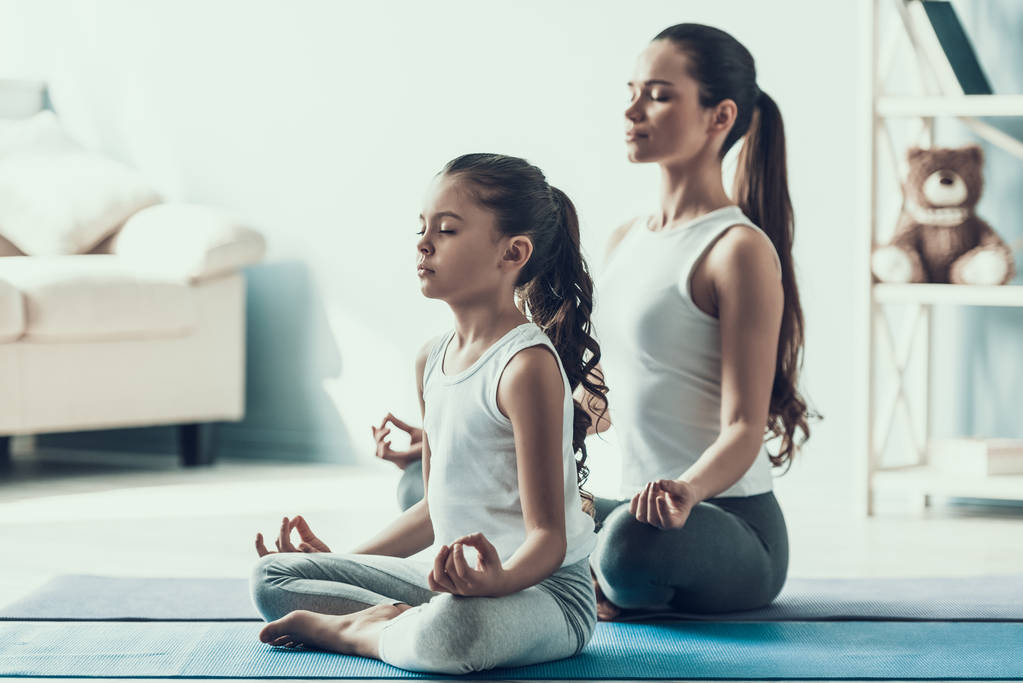 Jonge vrouw en een meisje doen Yoga vormen. Mooie jonge moeder en schattig dochtertje tijdens de oefening. Moeder en dochter samen Yoga oefenen thuis. Gezonde levensstijl - Foto, afbeelding