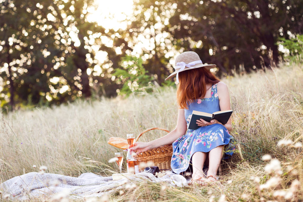Verano - Picnic provenzal en el prado. niña sentada leyendo un libro y cerca de una cesta de picnic y baguette, vino, vasos, uvas y rollo
 - Foto, imagen