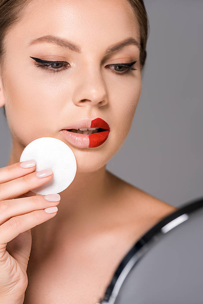 portrait de jeune femme avec rouge à lèvres sur la moitié des lèvres et éponge regardant miroir isolé sur gris
 - Photo, image