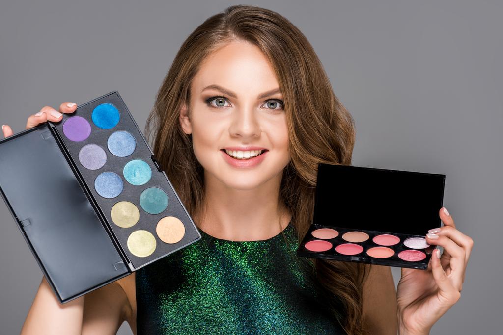 portrait of smiling woman with eyeshadows palettes isolated on grey - Photo, Image