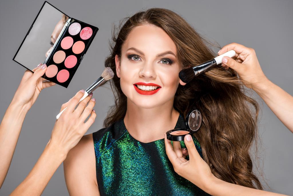 partial view of makeup artists with cosmetics and beautiful smiling woman isolated on grey - Photo, Image