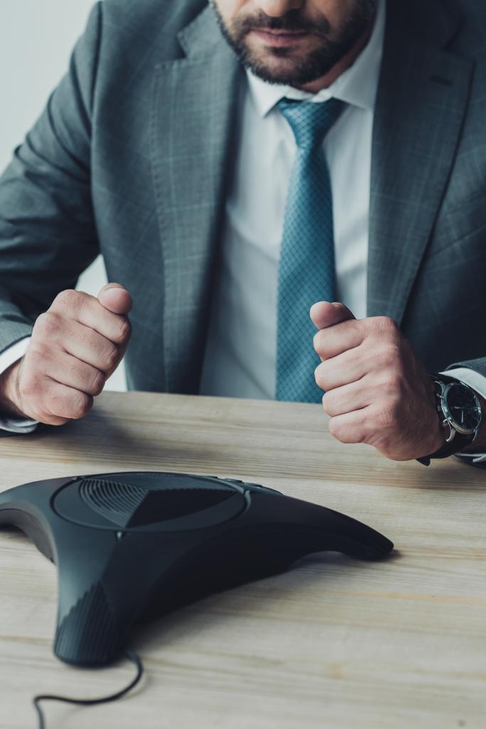 обрезанный снимок неудавшегося бизнесмена, сидящего перед телефоном и сжимающего кулаки в офисе
 - Фото, изображение