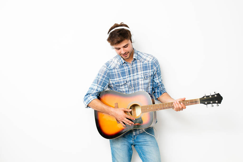 hobby para chicos. hombre tocando la guitarra con auriculares en la cabeza, disfrutando de su tiempo libre en su propia casa, haciendo lo que le gusta, sobre fondo blanco
 - Foto, imagen