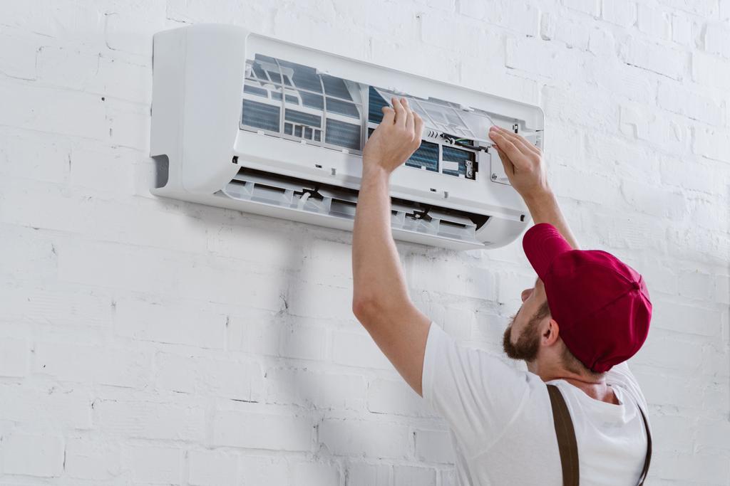 jovem reparador mudando filtro para ar condicionado pendurado na parede de tijolo branco
 - Foto, Imagem