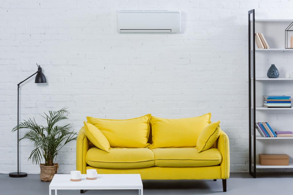 інтер'єр сучасної вітальні з жовтим диваном і кондиціонером, що звисає на білій стіні
 - Фото, зображення