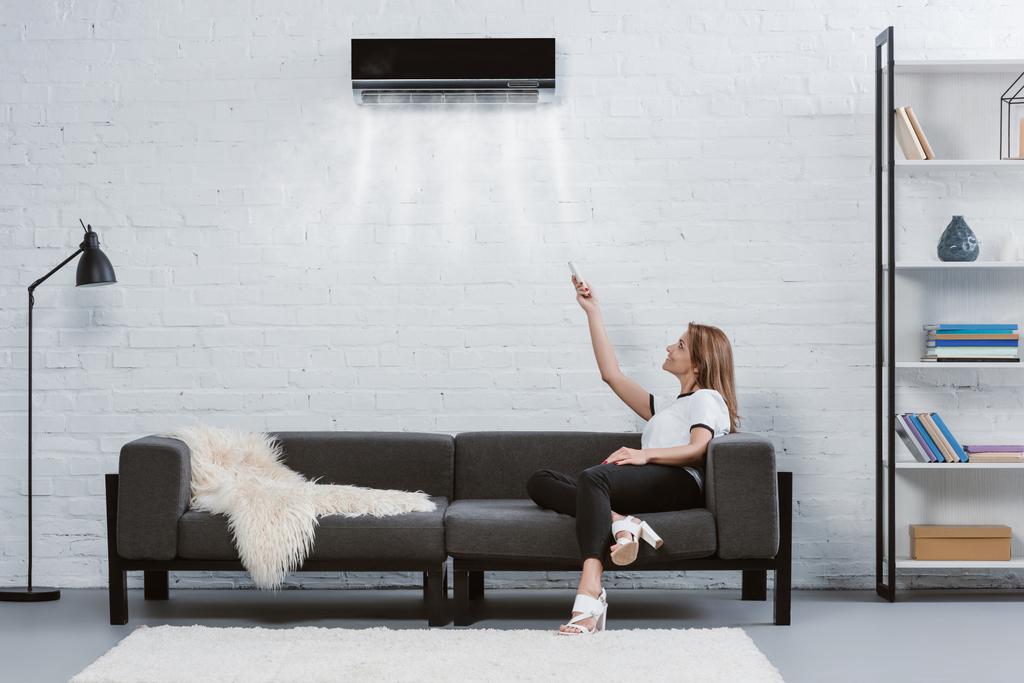 heureuse jeune femme pointant vers climatiseur suspendu au mur avec télécommande
 - Photo, image