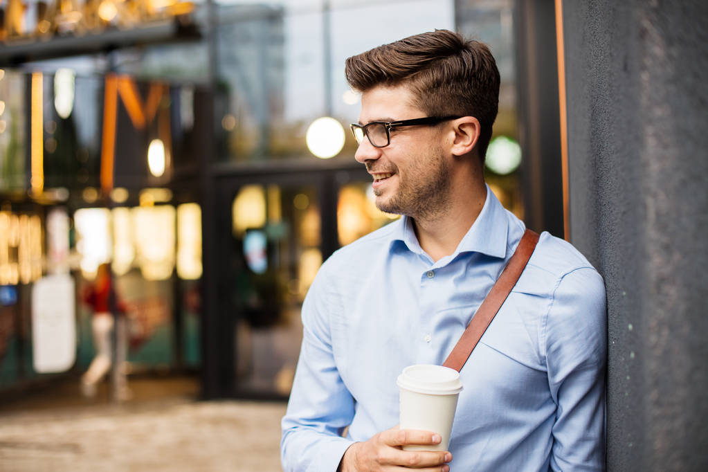 pausa para o café. bonito inteligente casual homem com óculos e bolsa de couro tendo um tomar café na área urbana fora
 - Foto, Imagem