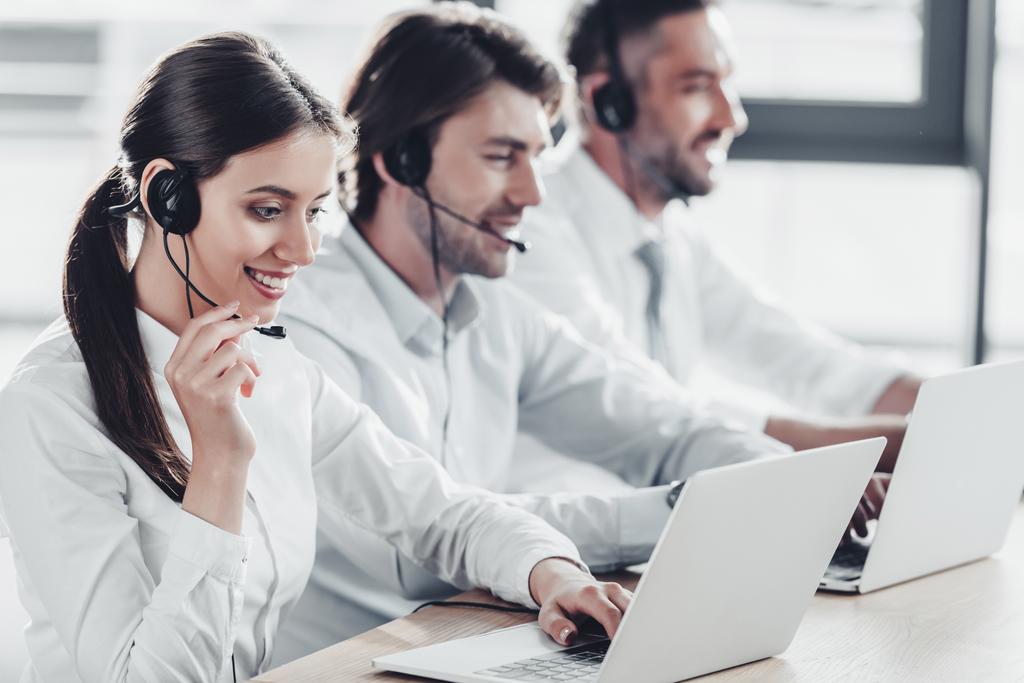 gerentes de centro de llamadas sonrientes en camisas blancas trabajando juntos mientras están sentados en fila en la oficina moderna
 - Foto, imagen