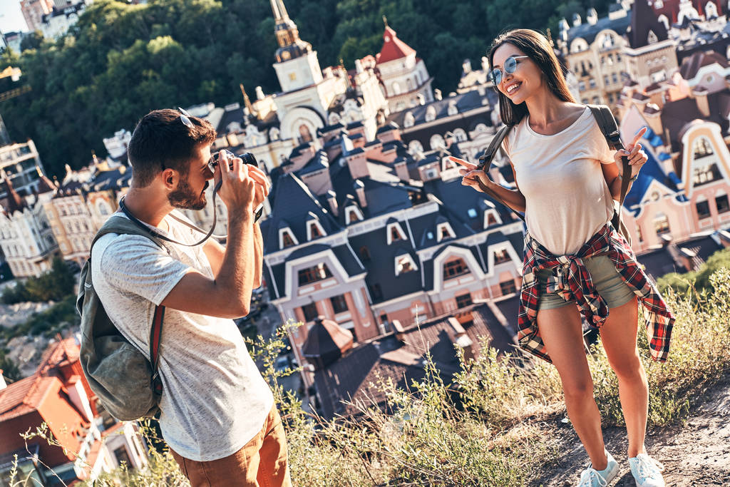 ο άνθρωπος που φωτογραφίζει φίλη ευτυχής ενώ στέκεται πάνω σε λόφο, πόλη σπίτια σε φόντο  - Φωτογραφία, εικόνα