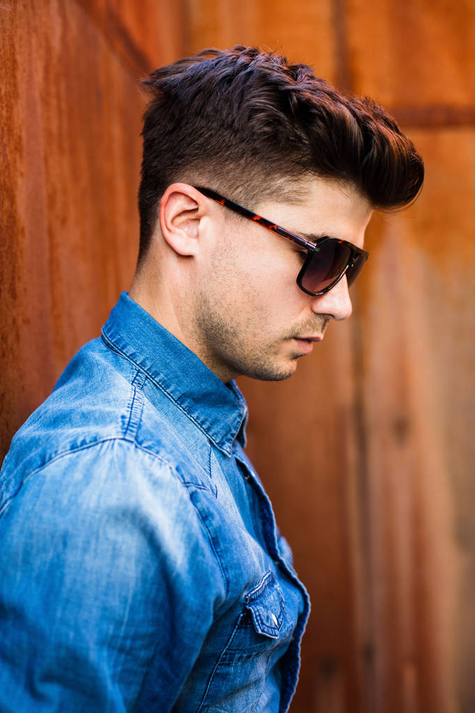 close up portrait of a sexy man with suglasses and jeans shirt on a rusty background, looking confident - Photo, Image