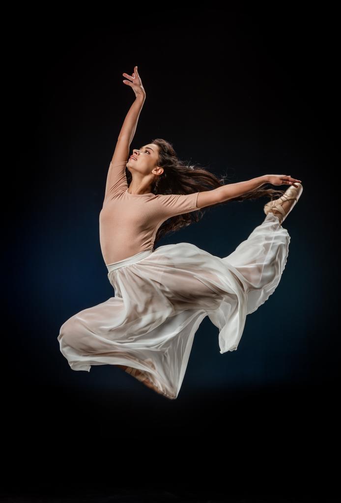 junge Ballerina in eleganter Kleidung springt vor dunklem Hintergrund - Foto, Bild