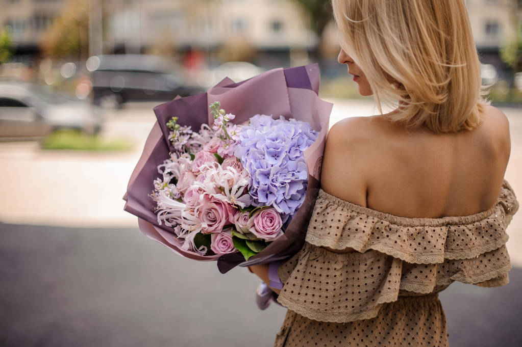 Hát Nézd, szőke fiatal nő a gazdaság egy romantikus virágcsokor, lila tónusú bézs ruha - Fotó, kép