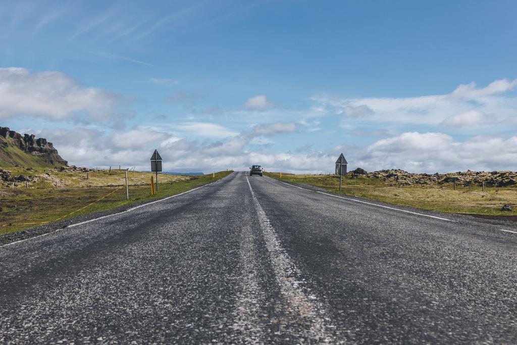 estrada com carro em terras altas sob céu azul nublado na Islândia
  - Foto, Imagem