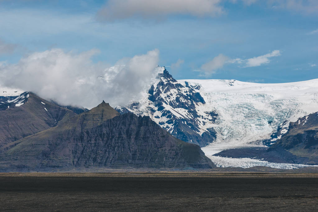 schöne Landschaft mit schneebedeckten Bergen unter blauem bewölkten Himmel in Island - Foto, Bild