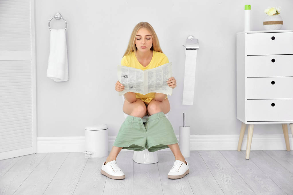 Jonge vrouw krant lezen zittend op de wc-pot thuis - Foto, afbeelding