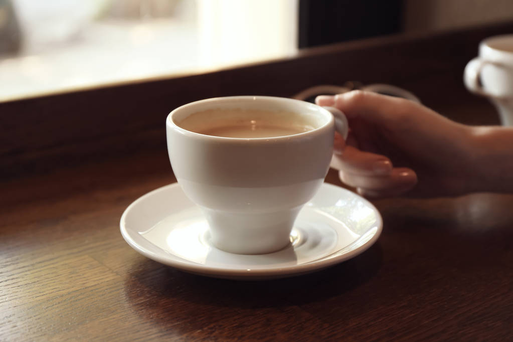 Жінка з чашкою свіжої ароматичної кави за столом
 - Фото, зображення