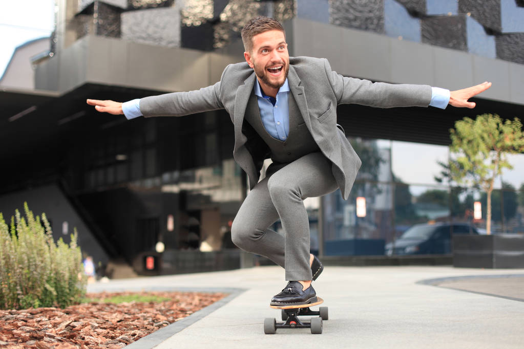 Jovem empresário confiante em terno de negócios em longboard apressando-se para seu escritório, na rua na cidade
 - Foto, Imagem