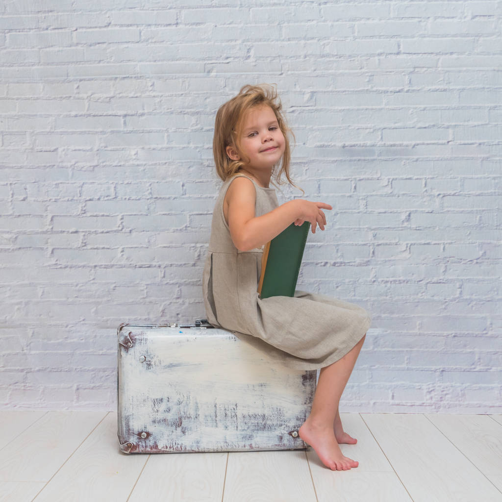 Dziewczyna, dziecko w stroju na tle ściany cegły z walizki, z książką - Zdjęcie, obraz