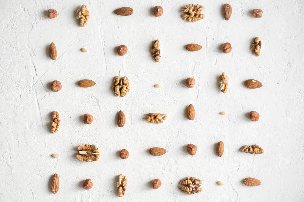 Various nuts (walnuts, hazelnuts, almonds and pine nuts) repetition on white background as pattern, flat lay with copy space. - Photo, Image