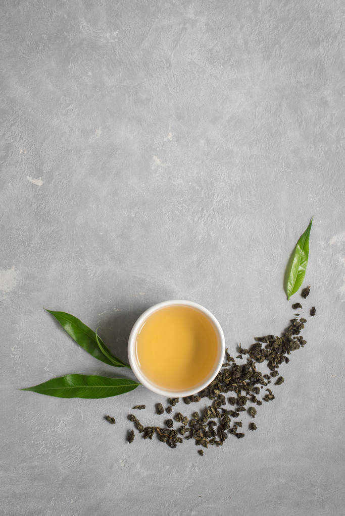 Green tea in ceramic cup, dry green oolong tea and tea leaves on grey stone table, top view, copy space. - Photo, Image