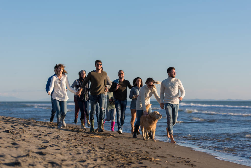 группа молодых друзей проводят день вместе, бегая по пляжу в осенний день - Фото, изображение