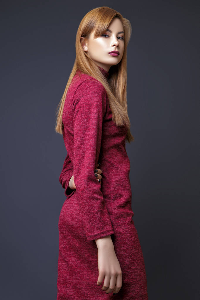 Милая молодая азиатка с рыжими волосами, одетая в бардовое платье, позирующая в студии на черном фоне
. - Фото, изображение